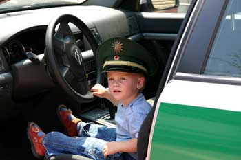 Das Bild zeigt einen kleinen Jungen mit Polizeimütze auf dem Fahrersitz eines Polizeiautos