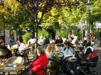 Das Bild zeigt ein gut besuchtes Cafe bei schönem Wetter