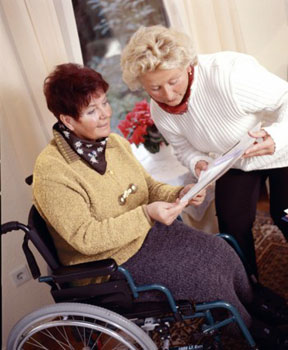 Das Bild zeigt eine Dame im Rollstuhl, die von einer Pflegerin betreuut wird