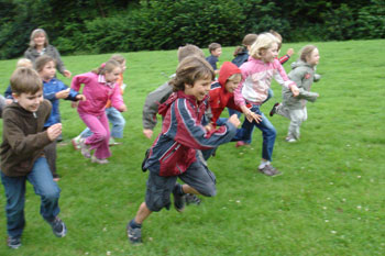 Das Bild zeigt Kinder, die fröhlich über die Wiese laufen